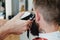Handsome bearded man in barbershop. Barber cuts hair with elect