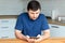 Handsome bearded man in a blue T-shirt sits behind a wooden table and reads an electronic book against a blurred background