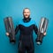 Handsome bearded man in diver suit smiling and holding flippers on blue background