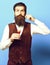 Handsome bearded man with long beard and mustache on surprised face tasting glass of alcoholic shot in vintage suede