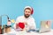 Handsome bearded man office worker in santa claus hat sitting at workplace and signing postcards, congratulating with winter