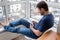 Handsome bearded relaxing man in a blue jeans and t-shirt reading an electronic book on digital device on the balcony