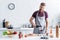 handsome bearded young man in apron pouring wine and smiling at camera while cooking