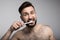 handsome bearded young man brushing teeth and looking at camera