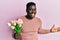Handsome black man holding bouquet of pink tulips flowers celebrating victory with happy smile and winner expression with raised