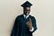 Handsome black man wearing graduation cap and ceremony robe beckoning come here gesture with hand inviting welcoming happy and