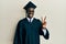 Handsome black man wearing graduation cap and ceremony robe showing and pointing up with fingers number two while smiling