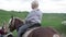 A handsome blond boy rides a horse along the river at sunset.