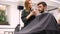 Handsome blue eyed man sitting in barber shop. Hairstylist Hairdresser Woman cutting his hair. Female barber.