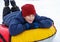 Handsome boy in blue jacket, red hat has fun on his winter holidays. Makes snowman, sledding