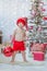 Handsome boy in red Santa Claus warm hat with big red Christmas tree toy ball celebrating New Year close to xmas tree