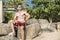 A handsome and buff asian man wearing shades, board shorts and flipflops on a rock while at a tropical resort