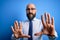 Handsome business bald man with beard wearing elegant tie and glasses over blue background afraid and terrified with fear