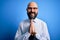 Handsome business bald man with beard wearing elegant tie and glasses over blue background praying with hands together asking for