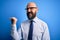 Handsome business bald man with beard wearing elegant tie and glasses over blue background smiling with happy face looking and