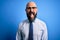 Handsome business bald man with beard wearing elegant tie and glasses over blue background sticking tongue out happy with funny