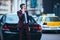 Handsome businessman entrepreneur standing proudly next to his parked limo at the middle of the business center