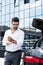 handsome businessman in eyeglasses rolling sleeves of white shirt near car trunk