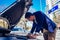 A handsome businessman wearing blue blazer lifting up the hood of his car and checking the oil level on a sunny day parked on a