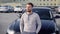 Handsome caucasian man is sitting on a hood of his big black car and thinking in parking area in summer evening