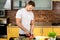 Handsome caucasian man in white tshirt slices vegetables for salad. A man standing in the kitchen at home