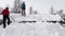 Handsome Caucasian teenager and mature man with shovels remove snow from roof of totally snow covered house, cabin in mountains.