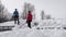 Handsome Caucasian teenager and mature man with shovels remove snow from roof of totally snow covered house, cabin in mountains.