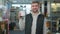 Handsome cheerful employee with brown eyes and toothy smile posing with tin of paint in hardware store. Portrait of