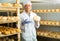 Handsome cheese maker checking aging process of goat cheese standing at small cellar.