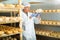 Handsome cheese maker checking aging process of goat cheese standing at small cellar.