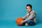 Handsome child, basketball player, sitting near a ball on blue background