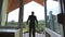 Handsome confident groom in black suit standing on the balcony leaning on railing and looking on the green forest on