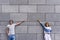 Handsome couple is pointing away and smiling, standing against gray wall.