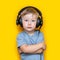 Handsome cute blonde little boy three years old in gaming black headphones. look at camera, grey eyes and grey t-shirt on yellow