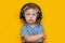 Handsome cute blonde little boy three years old in gaming black headphones. look at camera, grey eyes and grey t-shirt on yellow