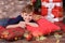 Handsome cute boy celebrating New Year Christmas alone close to xmas tree on red pillow posing in studio decoration wearing jeans