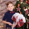 Handsome cute boy celebrating New Year Christmas alone close to xmas tree on red pillow posing in studio decoration wearing jeans