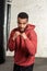 Handsome dark-skinned boxer in a sport suit is practicing the hooks and blows in front of the punching bags.