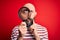 Handsome detective bald man with beard using magnifying glass over red background serious face thinking about question, very