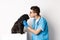 Handsome doctor veterinarian examining black pug, vet kissing and petting cute dog, white background