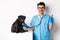 Handsome doctor veterinarian smiling, examining pet in vet clinic, checking pug dog with stethoscope, showing thumbs-up