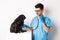 Handsome doctor veterinarian smiling, examining pet in vet clinic, checking pug dog with stethoscope, standing over