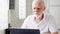 Handsome elderly senior man working on laptop computer at home. Remote freelance work on retirement