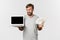 Handsome excited male freelancer showing laptop screen and money, standing over white background