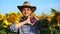 Handsome farmer man is showing love gesture in a sunflower field. Agriculture and nature concept