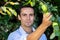 Handsome farmer picking green apples from tree and smiling at camera