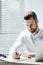 handsome focused businessman doing paperwork at workplace with laptop