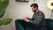 Handsome focused fashionable cuban man sitting on a sofa typing on his computer. Indoor shot