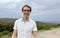 a handsome French or Spaniard man in a white shirt stands against the backdrop of mountains