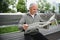 Handsome grandfather sits on a bench in the park and reads a newspaper. Senior gray-haired man.